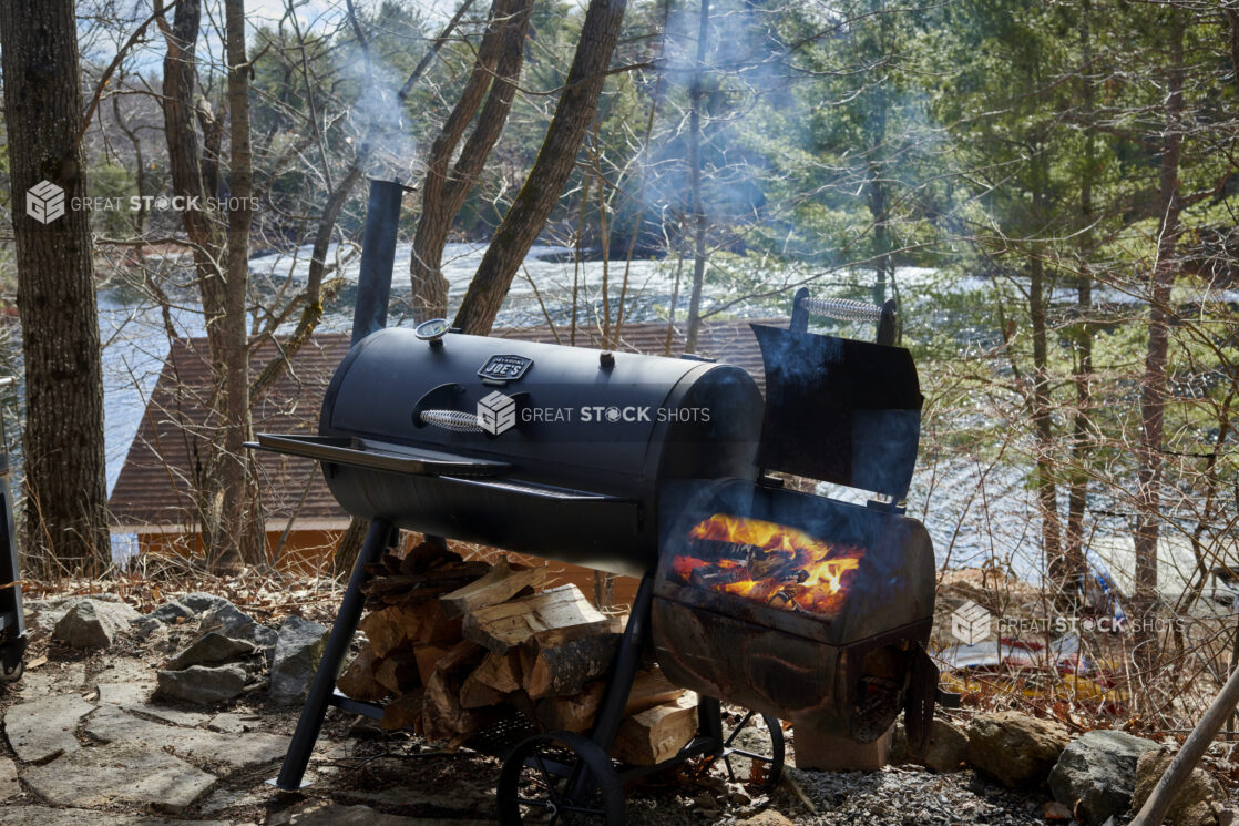 Charcoal Barrel Grill with Wood-Burning Smoker on a Hill Overlooking a Cottage on a Frozen Lake in Ontario, Canada