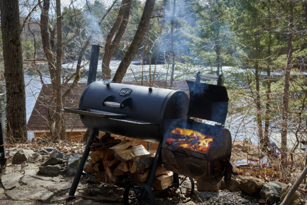 Charcoal Barrel Grill with Wood-Burning Smoker on a Hill Overlooking a Cottage on a Frozen Lake in Ontario, Canada
