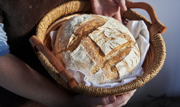 Woman's Hands Placing a Freshly Baked Sourdough Loaf into a Cloth-Lined Basket for Cooling
