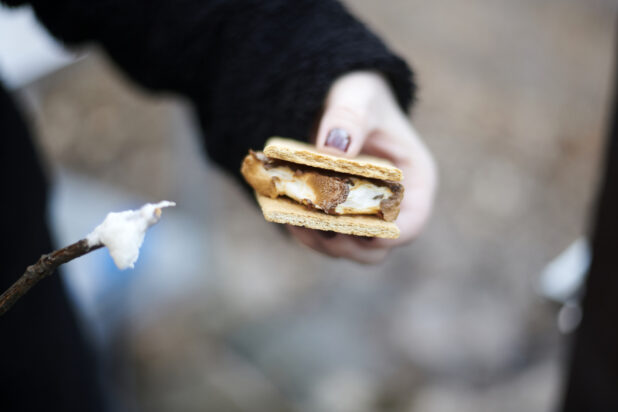 Close Up of a Person Sandwiching a Toasted Marshmallow Between Graham Crackers to Make a S’mores Treat in an Outdoor Setting