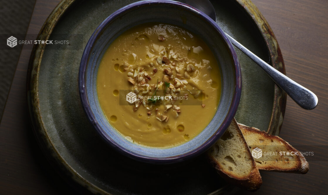 Overhead View of a Thick and Creamy Butternut Squash Soup in a Blue Ceramic Bowl with Sliced Baguette Toast on a Wooden Table