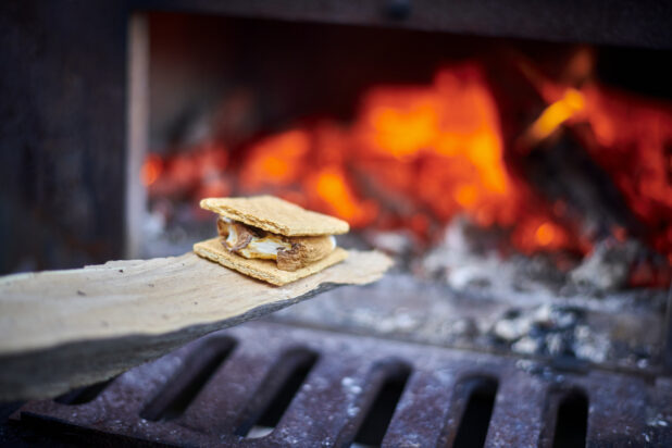Close Up of a S'mores Treat Being Toasted Near the Open Flame of a Wood-Burning Oven in an Outdoor Setting