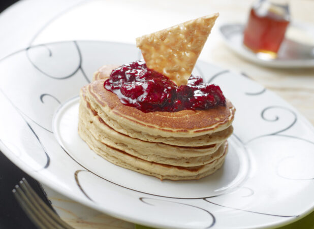 Stack of Thick Buttermilk Pancakes with a Berry Compote Topping on a White Ceramic Dish in a Restaurant Setting