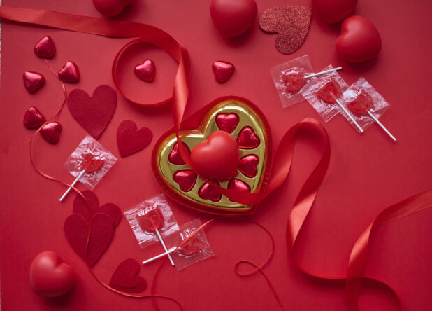 Overhead View of A Box of Heart-Shaped Chocolates Surrounded by Valentine’s Day Decorations on a Red Surface - Variation