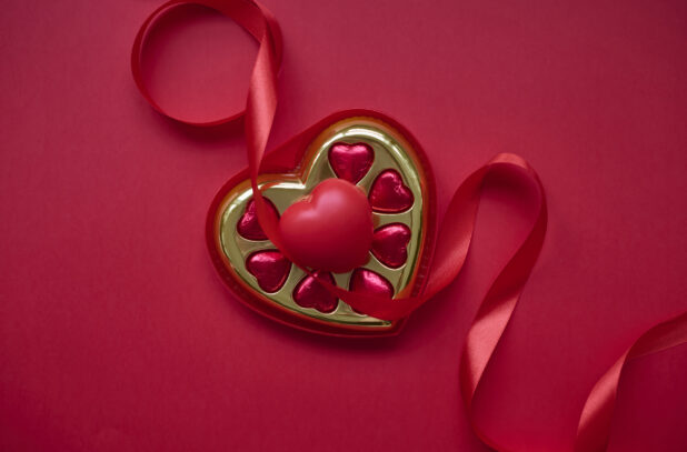 Overhead View of A Box of Heart-Shaped Chocolates and a Red Ribbon on a Red Surface