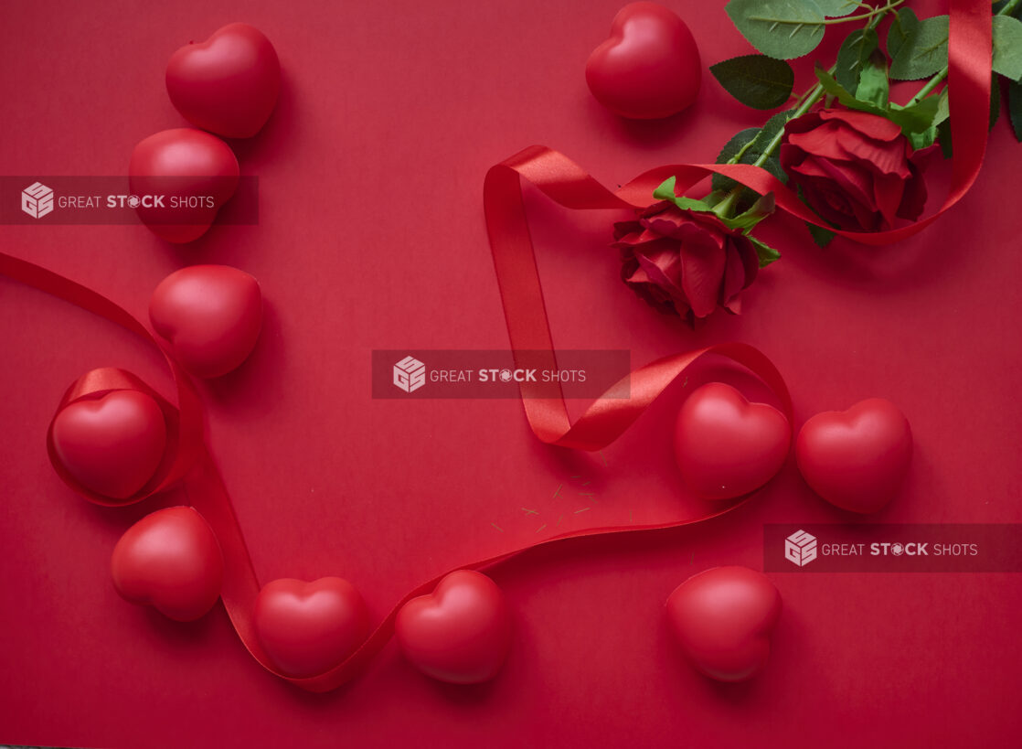 Overhead View of Red Heart Decorations, Red Roses and a Red Ribbon Arranged on a Red Surface