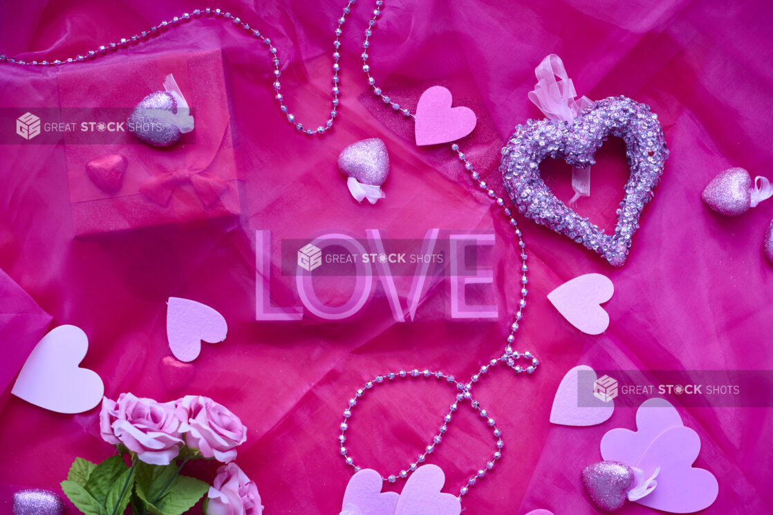 Overhead View of Valentine’s Day Decorations, Roses, Chocolate Hearts and a Gift Box on a Pink Table Cloth Surface