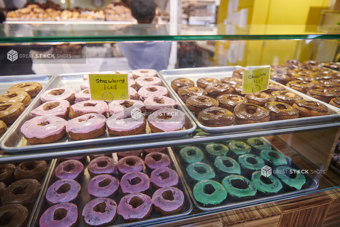 Showcase in a Donut Shop with Baking Pans Lined with Colourful Iced Donuts in an Indoor Market