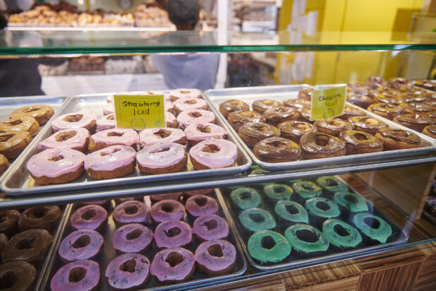 Showcase in a Donut Shop with Baking Pans Lined with Colourful Iced Donuts in an Indoor Market