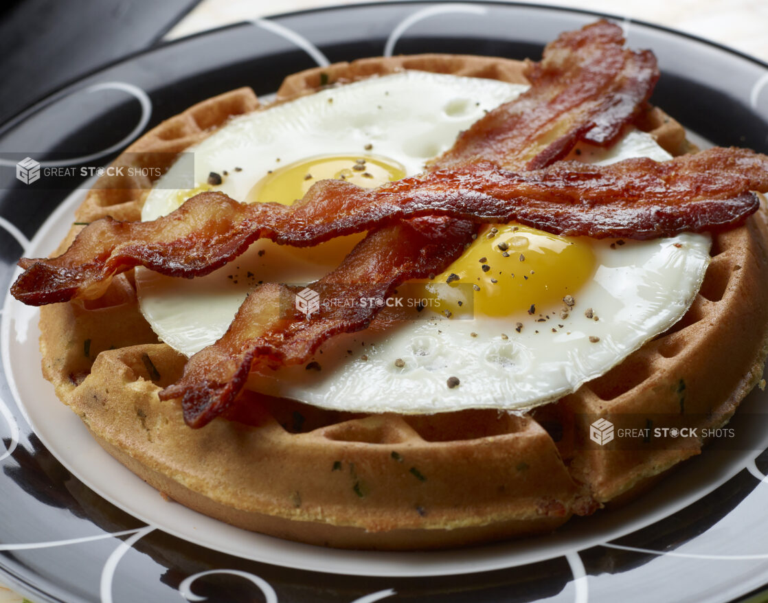 Close Up of a Savoury Waffle Topped with Two Fried Eggs and Strips of Bacon