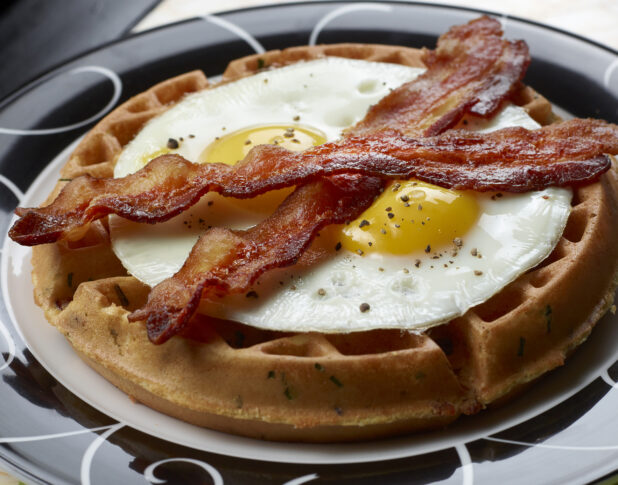 Close Up of a Savoury Waffle Topped with Two Fried Eggs and Strips of Bacon