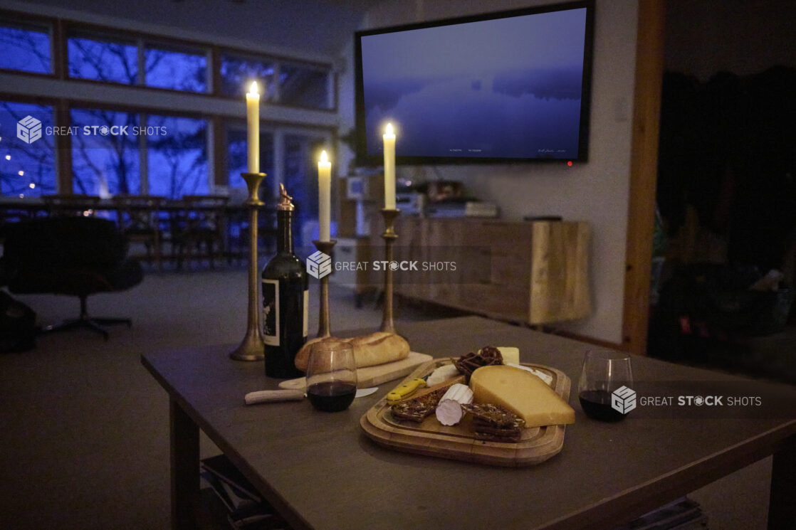 A Candlelit Spread of Cheese, Crackers and Bread with a Bottle of Red Wine in a Living Room Setting