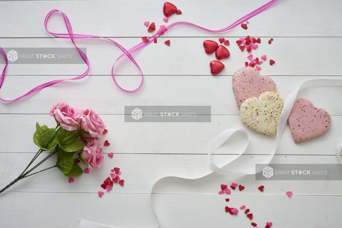 Overhead View of Heart Shaped Cookies, Pink Roses, Satin Ribbons and Heart Confetti on a White Painted Wood Table – Variation 2