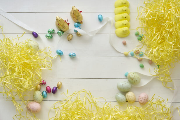 Overhead View of Assorted Chocolate Easter Eggs and Easter-Themed Sweets on a White Painted Wood Table with Yellow Stuffing Paper