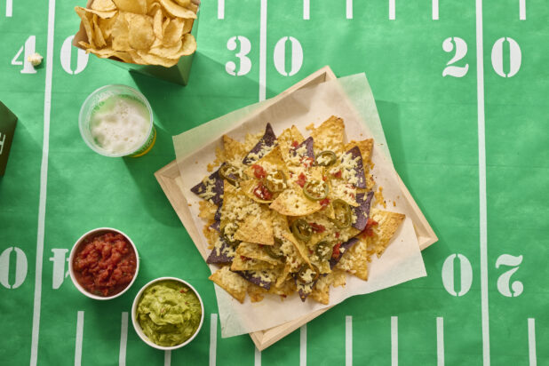 Overhead View of a Nacho Platter on a Square Wood Tray with Sides of Salsa, Guacamole on a Football Field Table Cloth