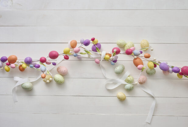 Overhead View of an Easter Egg Garland and Pastel-Coloured Easter Eggs on a White Painted Wood Table