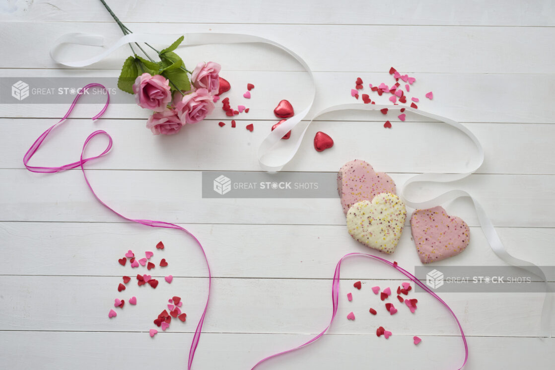 Overhead View of Heart Shaped Cookies, Pink Roses, Satin Ribbons and Heart Confetti on a White Painted Wood Table - Variation