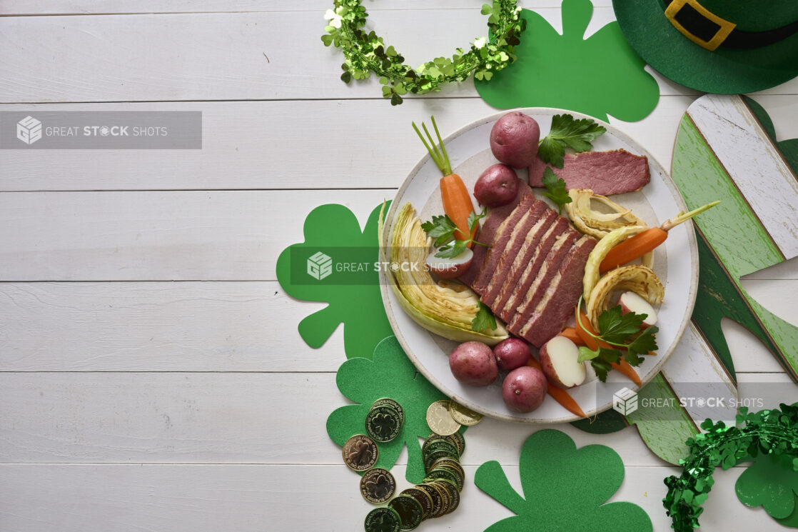 Overhead Shot of a Plate of Corned Beef and Cabbage, Carrots and Red Skinned Potatoes on a White Painted Wood Table Surrounded by St. Patrick’s Day Decorations - Variation