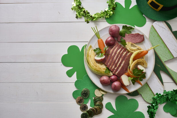 Overhead Shot of a Plate of Corned Beef and Cabbage, Carrots and Red Skinned Potatoes on a White Painted Wood Table Surrounded by St. Patrick’s Day Decorations - Variation
