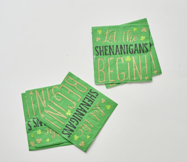 Green Paper Napkins with the Slogan "Let the Shenanigans Begin" for St. Patrick's Day Celebrations, Shot on White for Isolation