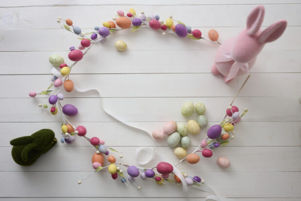 Overhead View of an Easter Egg Garland/Wreath, Easter Bunnies and Pastel-Coloured Easter Eggs on a White Painted Wood Table