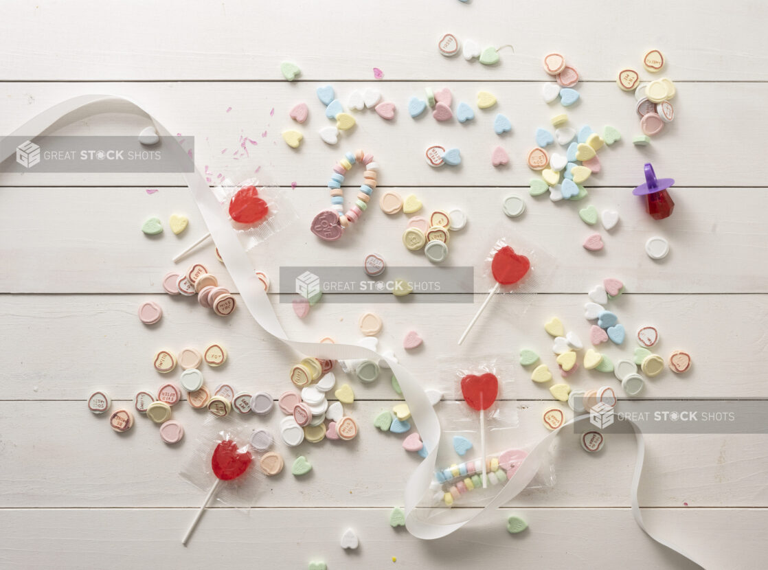 Overhead Shot of a White Painted Wood Tabletop with Candy Hearts and Heart-Shaped Lollipops Scattered
