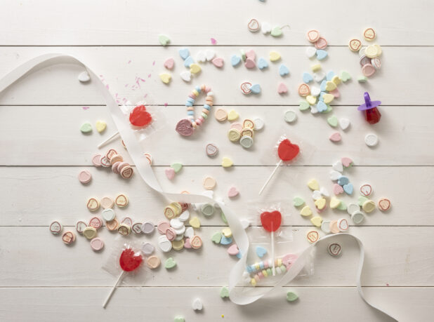 Overhead Shot of a White Painted Wood Tabletop with Candy Hearts and Heart-Shaped Lollipops Scattered