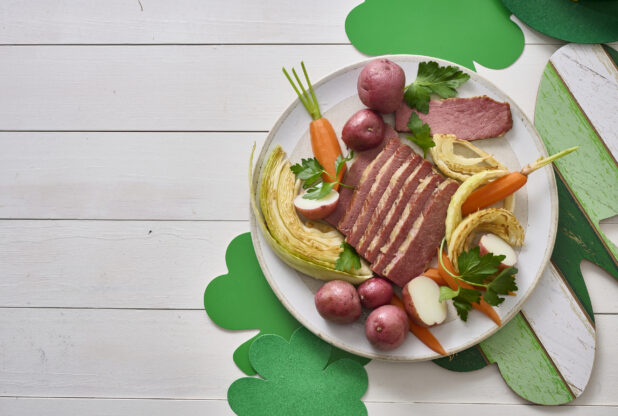 Overhead Shot a Plate of Corned Beef and Cabbage, Carrots and Red Skinned Potatoes on a White Painted Wood Table Surrounded by St. Patrick’s Day Decorations