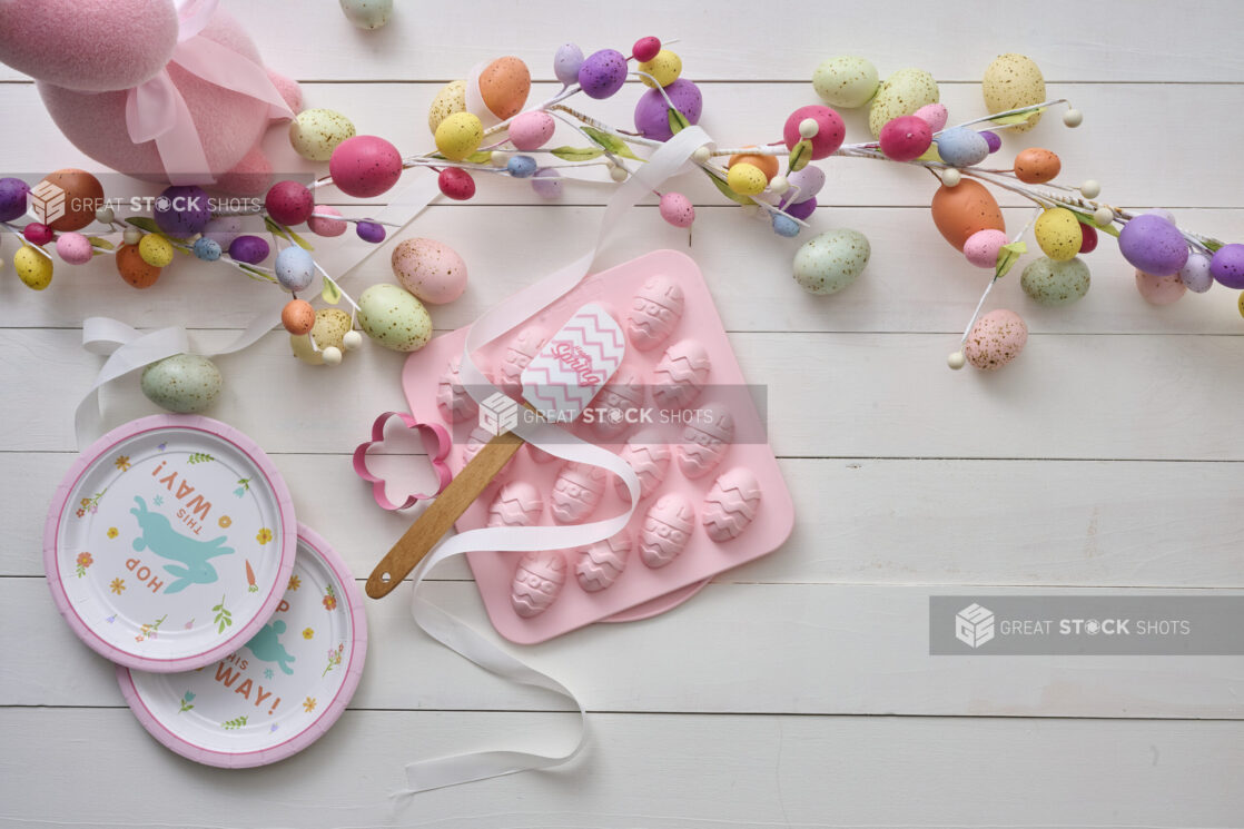 Overhead View of Easter Egg Decorations, Party Plates and a Pink Easter Egg Chocolate Mold on a White Painted Wood Table