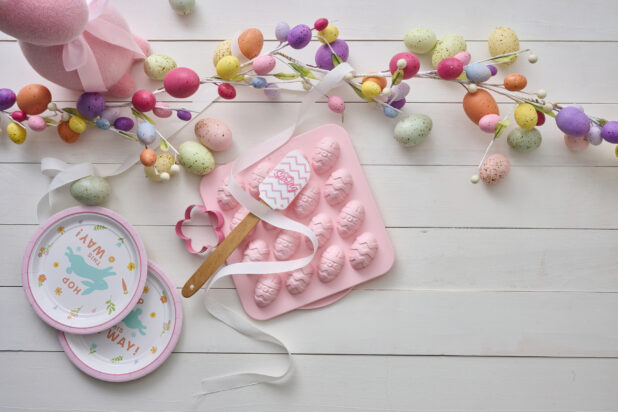 Overhead View of Easter Egg Decorations, Party Plates and a Pink Easter Egg Chocolate Mold on a White Painted Wood Table