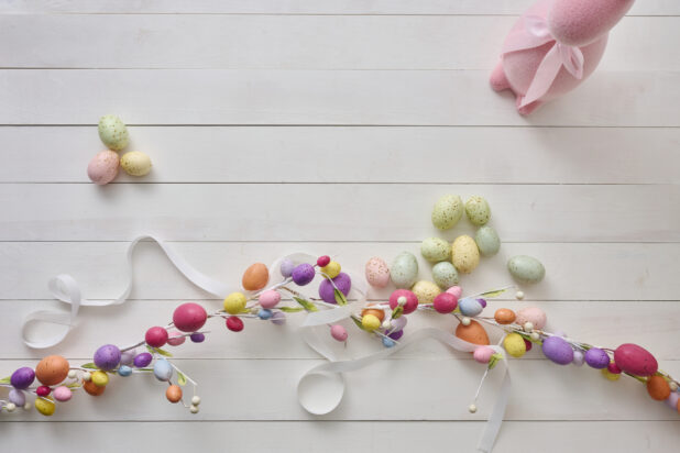 Overhead View of an Easter Egg Garland, Pink Easter Bunny and Pastel-Coloured Easter Eggs on a White Painted Wood Table