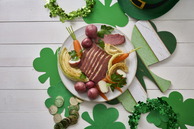 Overhead Shot of a Plate of Corned Beef and Cabbage, Carrots and Red Skinned Potatoes on a White Painted Wood Table Surrounded by St. Patrick’s Day Decorations – Variation 2