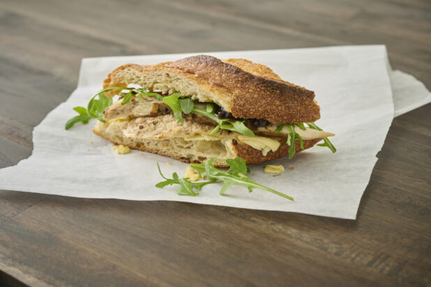 Roasted Chicken Breast and Baby Arugula on Sliced Toasted Baguette on a White Parchment Paper on a Dark Wooden Table