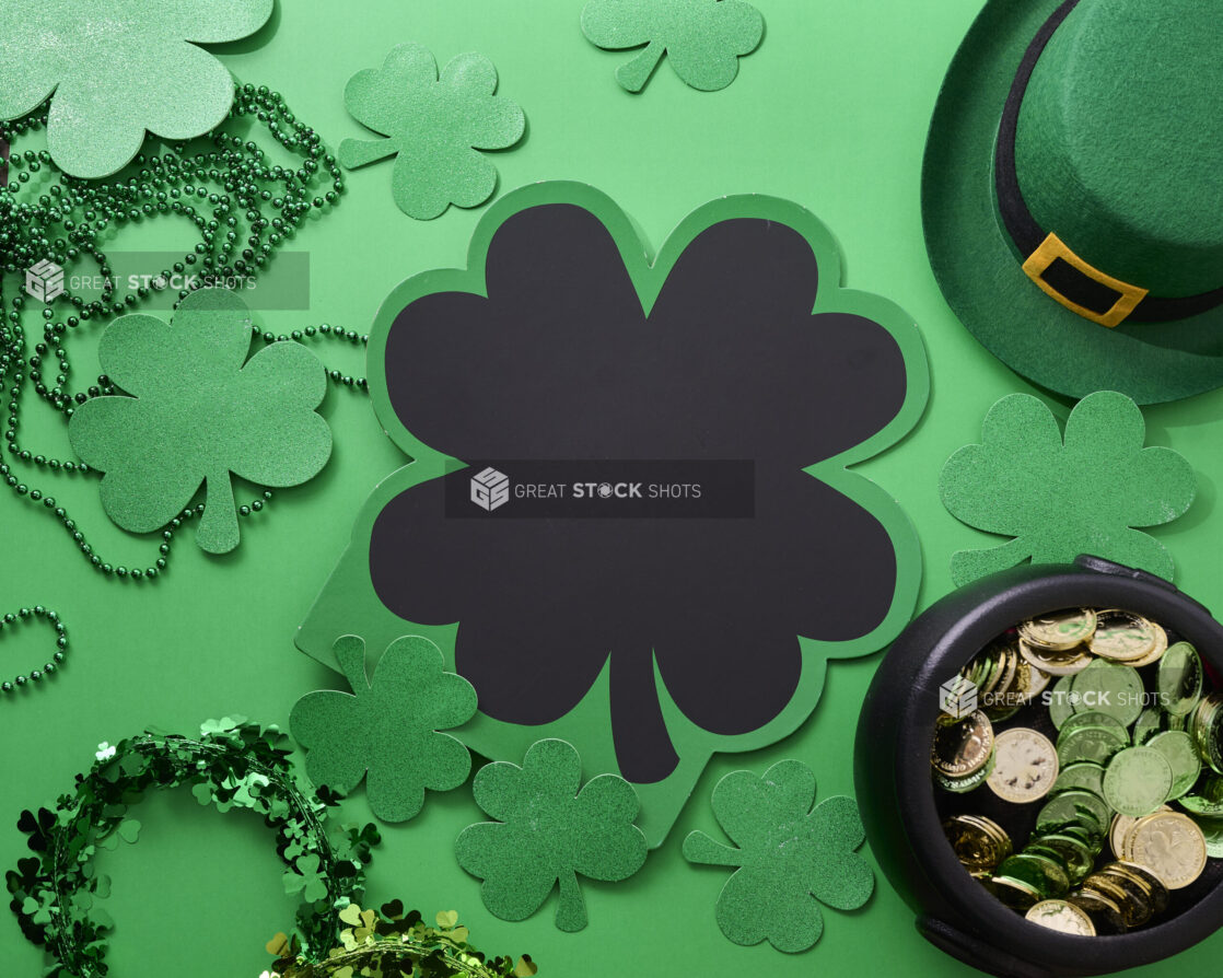 Overhead View of a Shamrock-Shaped Chalkboard Sign Surrounded by Assorted St. Patrick’s Day Decorations on a Green Background