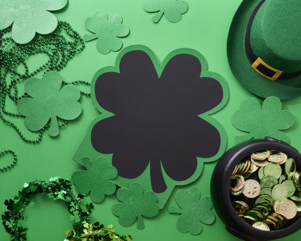 Overhead View of a Shamrock-Shaped Chalkboard Sign Surrounded by Assorted St. Patrick’s Day Decorations on a Green Background