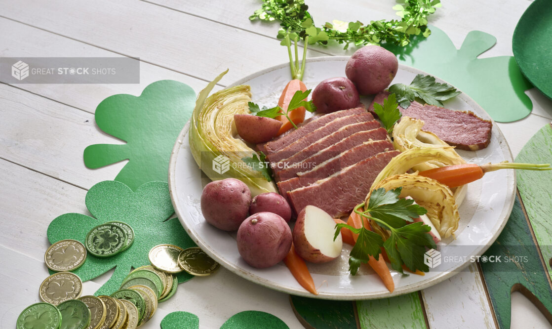 Plate of Corned Beef and Cabbage with Carrots and Red Skinned Potatoes on a White Painted Wood Table Surrounded by St. Patrick’s Day Decorations - Variation