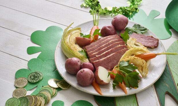 Plate of Corned Beef and Cabbage with Carrots and Red Skinned Potatoes on a White Painted Wood Table Surrounded by St. Patrick’s Day Decorations - Variation