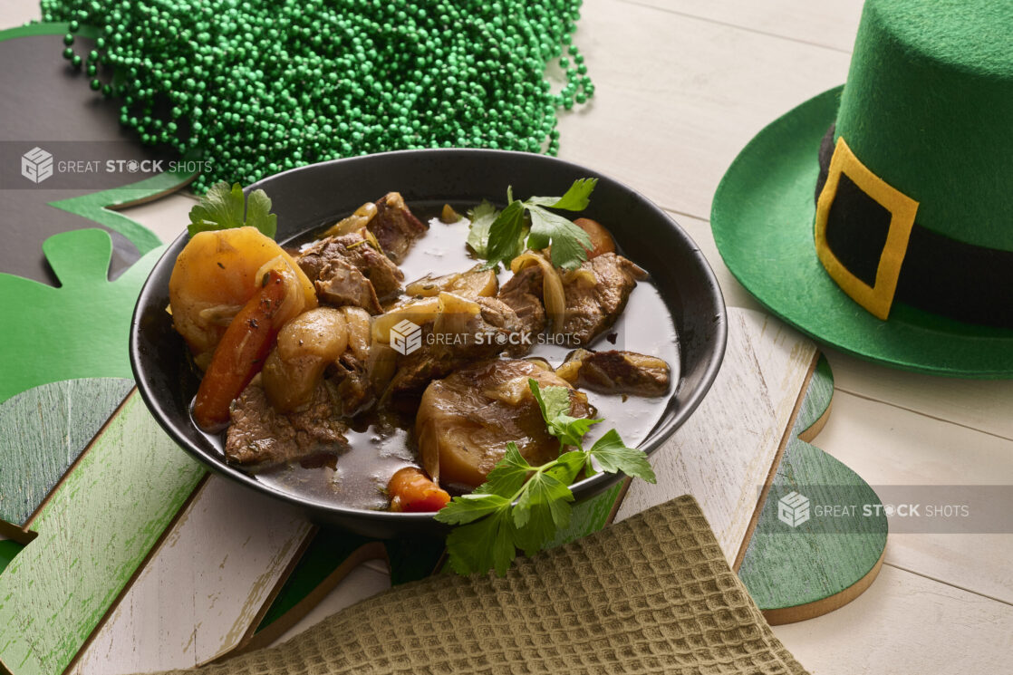 Close Up of a Large Black Bowl of Irish Stew With Carrots, Potatoes and Beef Surrounded by St. Patrick's Day Decorations