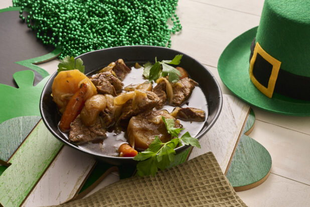 Close Up of a Large Black Bowl of Irish Stew With Carrots, Potatoes and Beef Surrounded by St. Patrick's Day Decorations