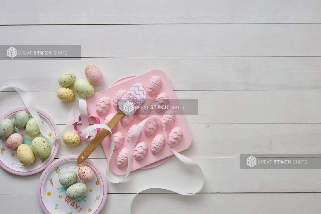 Overhead View of Pastel-Coloured Easter Eggs and a Pink Easter Egg Chocolate Mold on a White Painted Wood Table