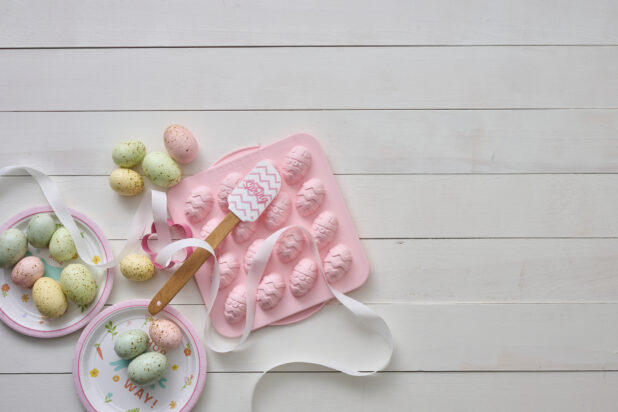 Overhead View of Pastel-Coloured Easter Eggs and a Pink Easter Egg Chocolate Mold on a White Painted Wood Table