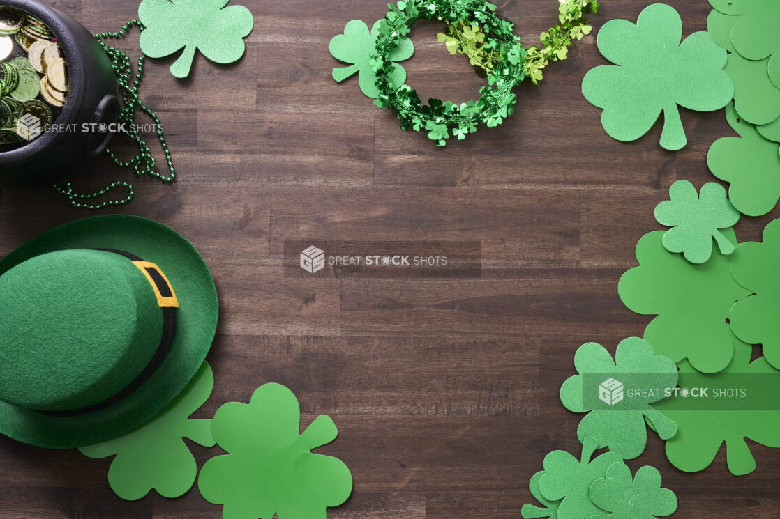 Overhead View of an Assortment of St. Patrick’s Day Decorations – Shamrock Wreaths, Leprechaun Hat, Green Clover Clings and a Pot of Gold on a Dark Wood Background - Variation