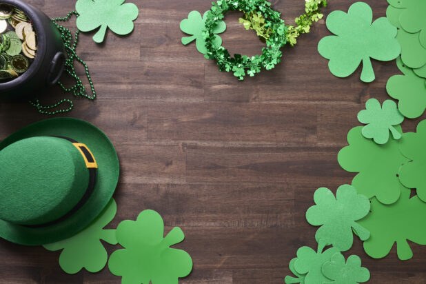 Overhead View of an Assortment of St. Patrick’s Day Decorations – Shamrock Wreaths, Leprechaun Hat, Green Clover Clings and a Pot of Gold on a Dark Wood Background - Variation
