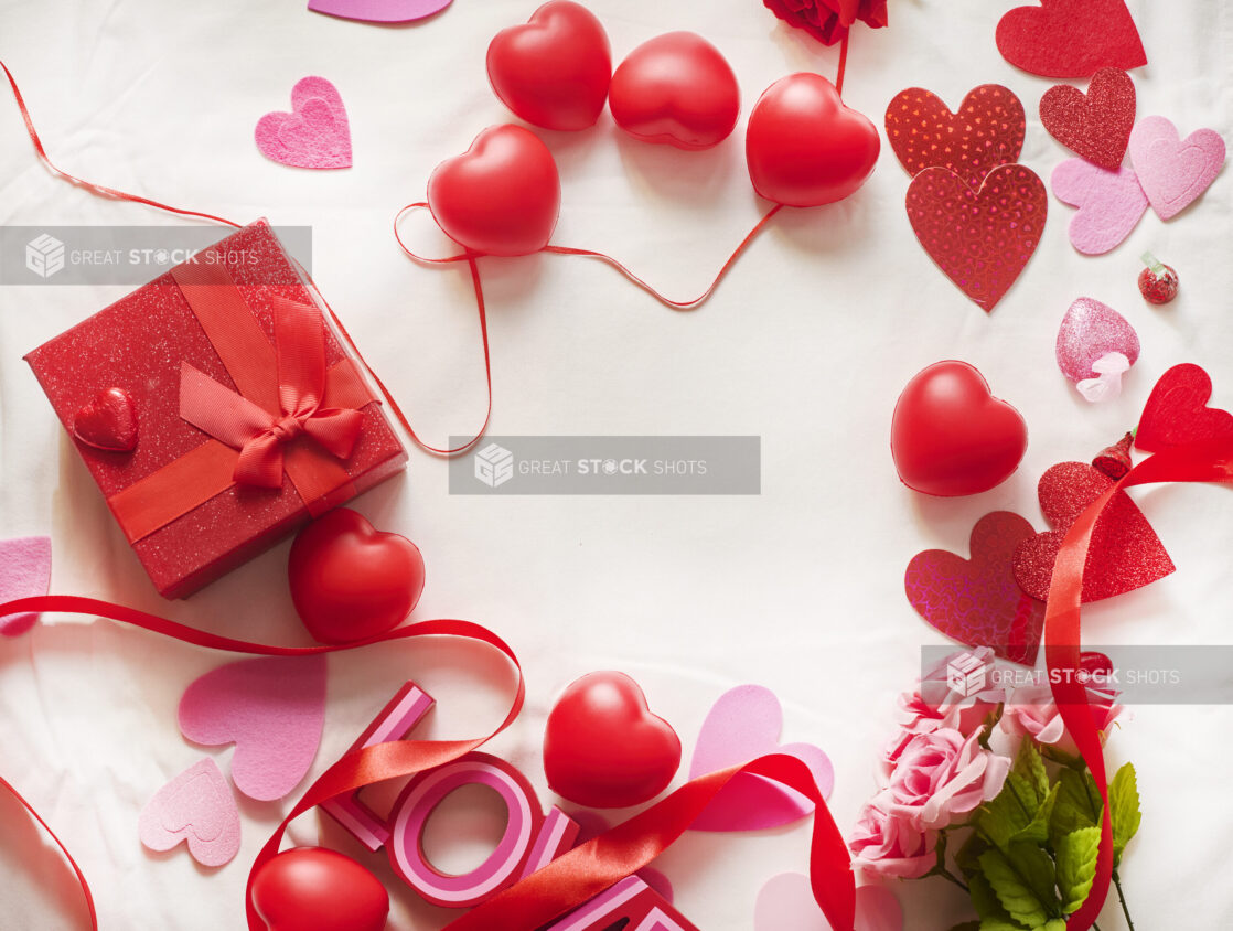 Overhead View of Valentine's Day Decorations, Roses, Chocolate Hearts and a Gift Box on a White Table Cloth Surface