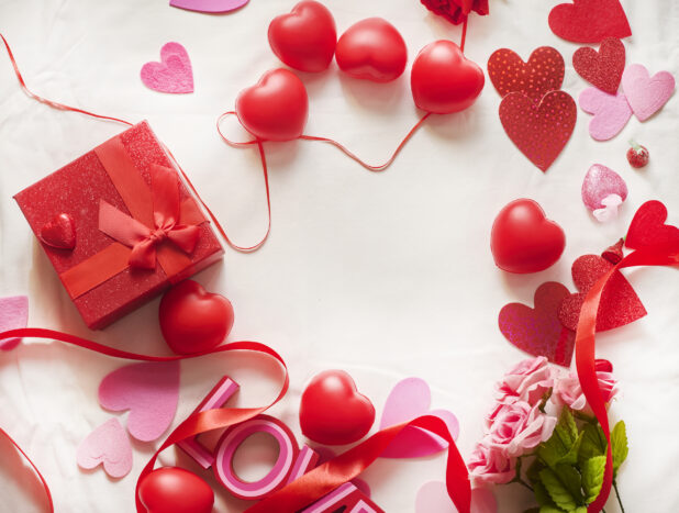 Overhead View of Valentine's Day Decorations, Roses, Chocolate Hearts and a Gift Box on a White Table Cloth Surface