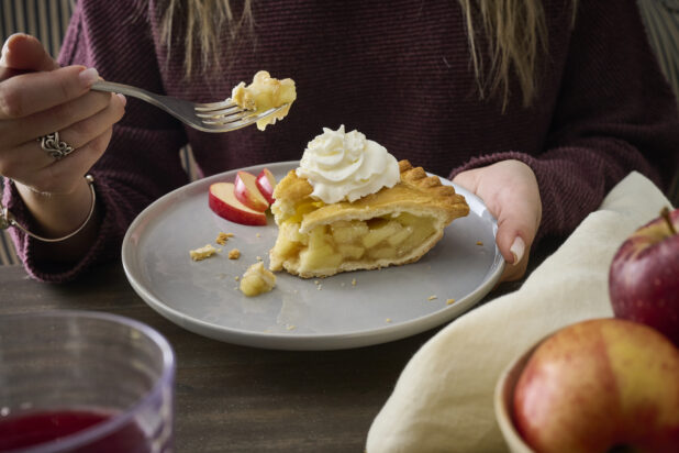 Person Eating a Apple Pie with Whipped Cream Garnish on a Grey Ceramic Dish in an Indoor Setting - Variation
