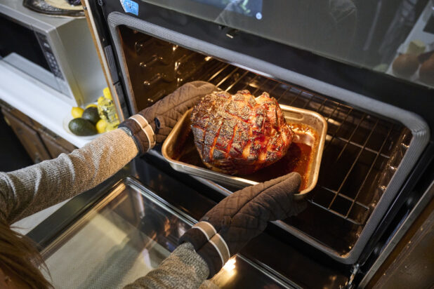 Hands Pulling a Roasted Ham Out of a Kitchen Oven in an Indoor Home Setting