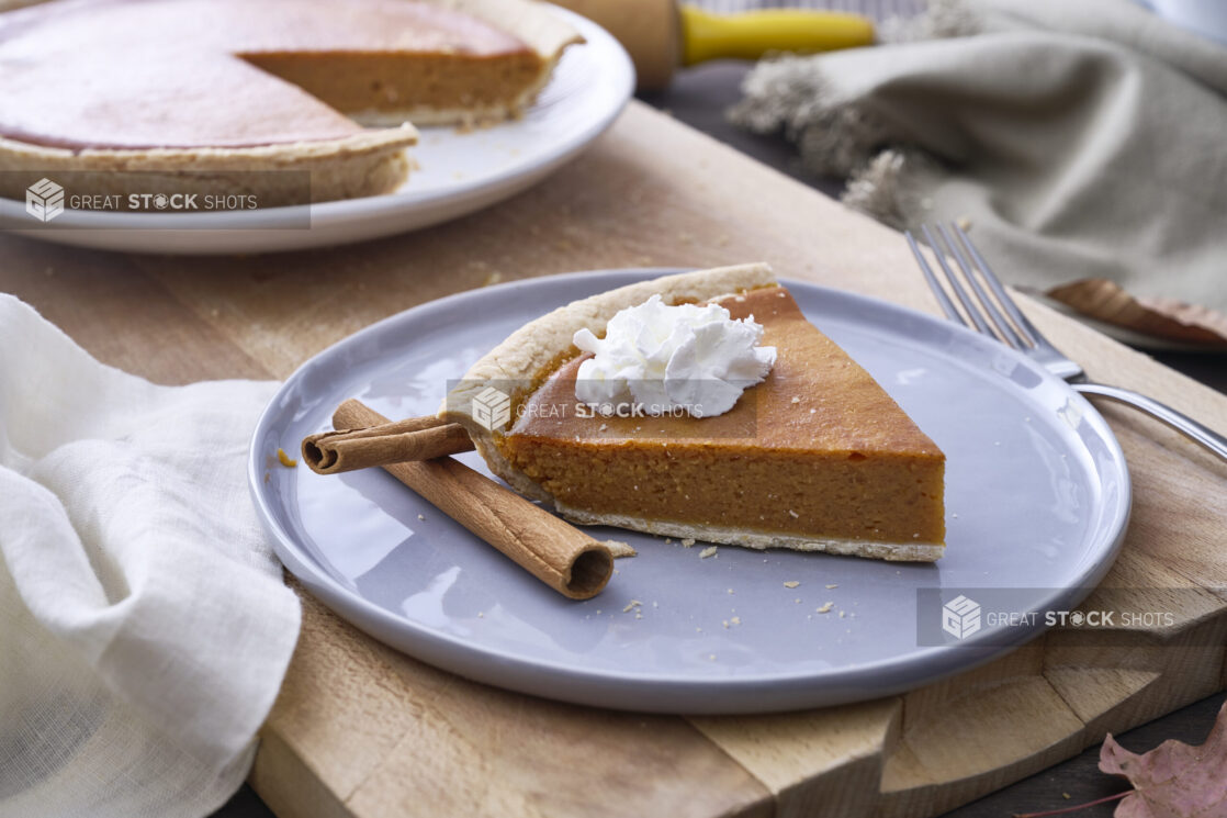 Slice of Pumpkin Pie with Whipped Cream Garnish and Cinnamon Sticks on a Grey Ceramic Dish