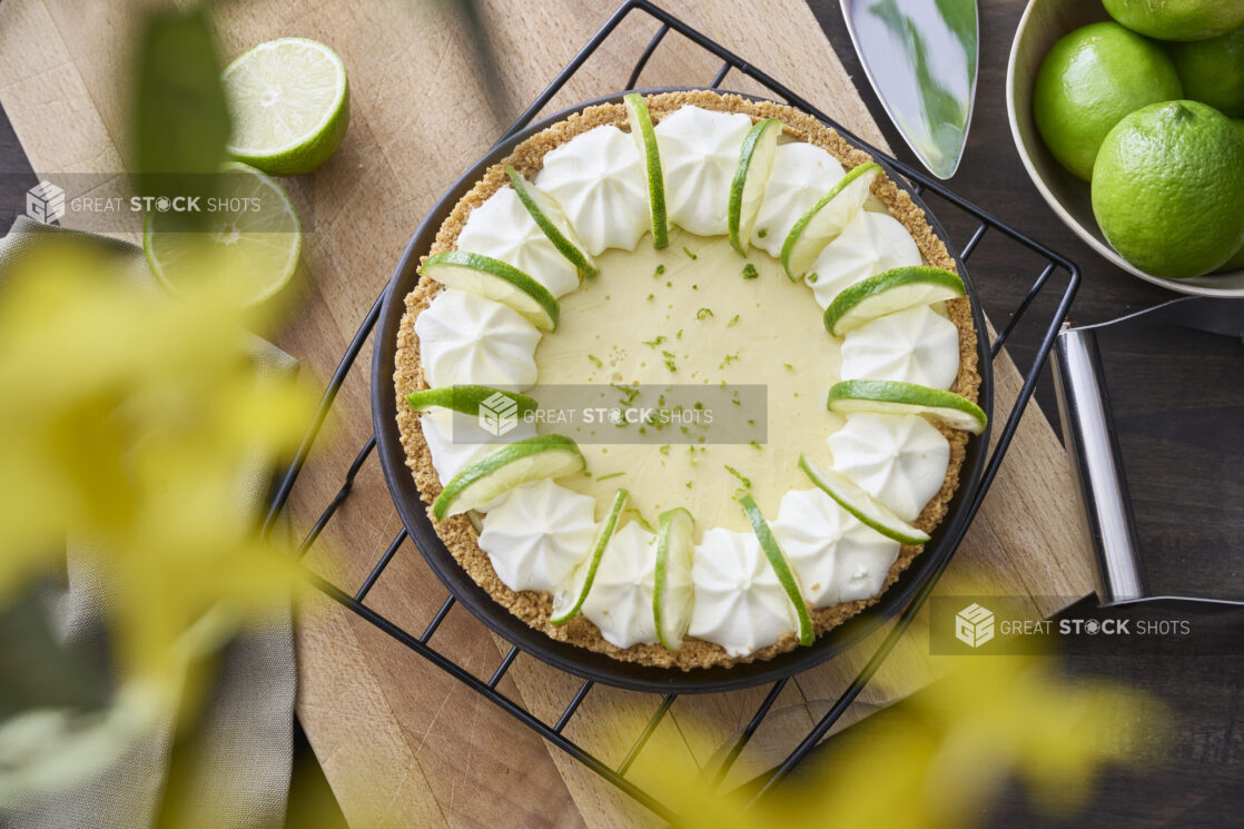 Overhead View of a Whole Key Lime Pie with Sliced Lime and Whipped Cream Garnish on a Cooling Rack in an Indoor Setting - Variation