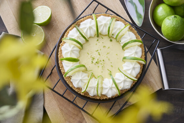 Overhead View of a Whole Key Lime Pie with Sliced Lime and Whipped Cream Garnish on a Cooling Rack in an Indoor Setting - Variation